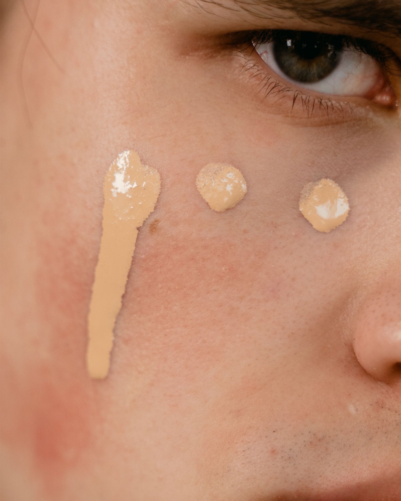 Close-up of foundation dots and a stripe on a man's cheek, below his eye
